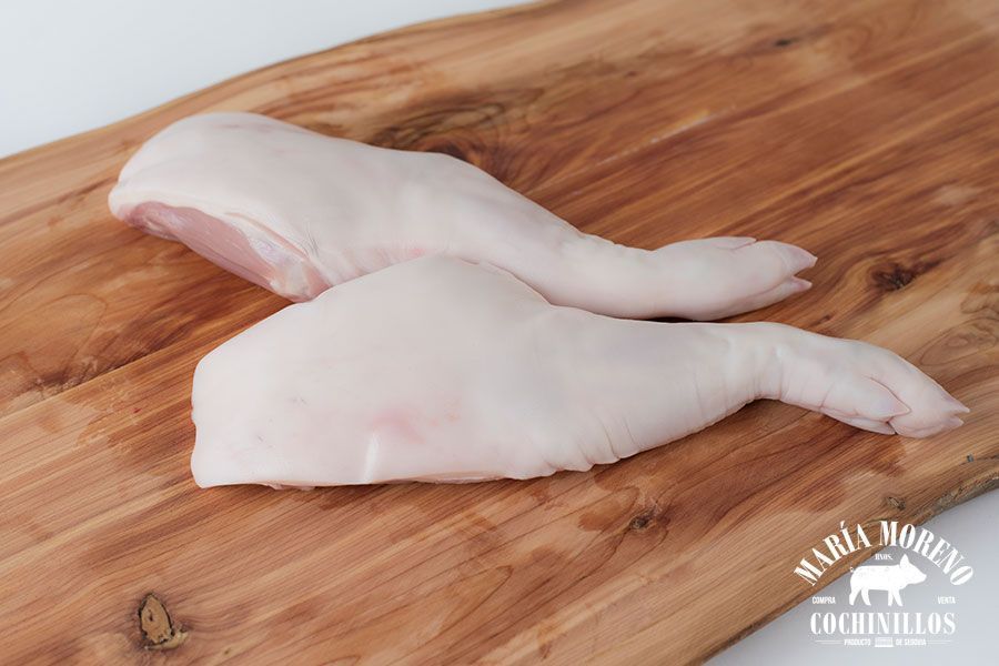 Dos paletillas de cochinillo de Segovia sobre una tabla de cortar de madera, con el logotipo «MARÍA MORENO COCHINILLOS» en la esquina inferior derecha: una opción perfecta para quienes quieran comprar paletillas de cochinillo de Segovia y disfrutar de sabores auténticos en casa.