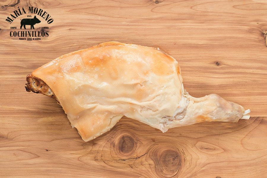 Un CUARTO de cochinillo de Segovia FRESCO y PREASADO, recién asado y con una piel dorada y crujiente, se exhibe sobre una superficie de madera, realzado por el logotipo de «Maria Moreno Cochinillos» en una esquina: una invitación irresistible a comprar cochinillo de Segovia y saborear un auténtico manjar español.